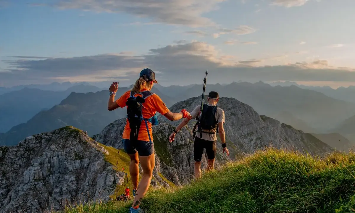 Dwie osoby w sportowym stroju, z plecakami i kijkami, biegną po górskim szlaku. Idealny przykład, jak się ubrać w góry na bieg.