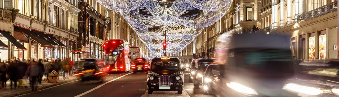 Julbelysning i London i december. Röda dubbeldäckare och taxibilar susar förbi på en livlig gata.