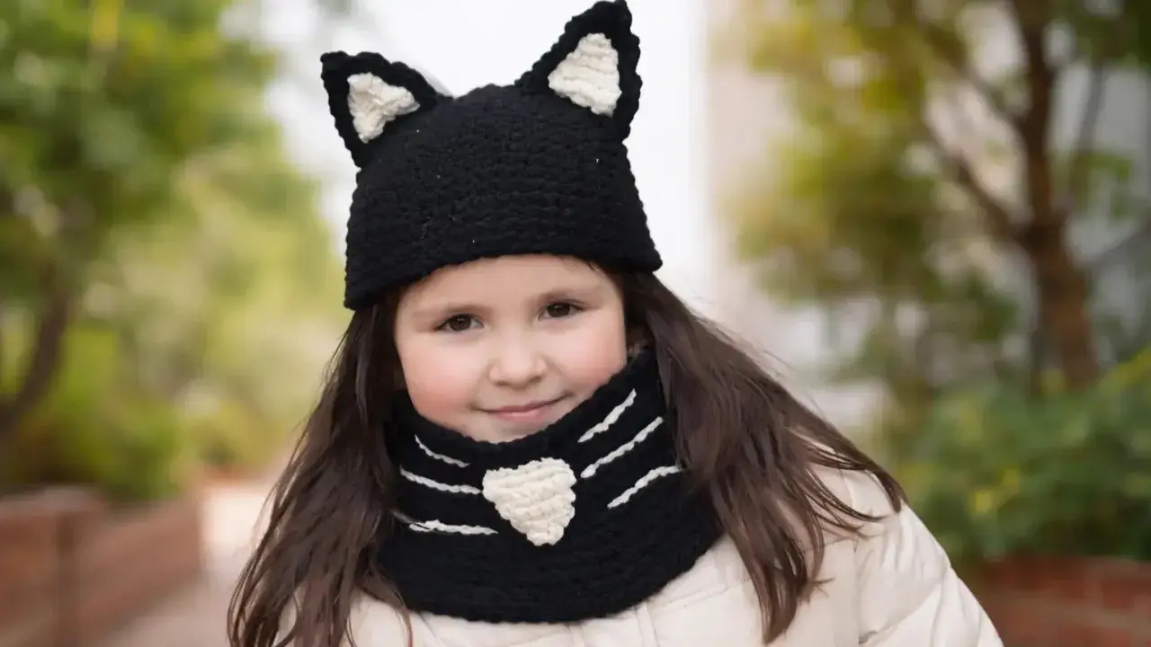 Niña sonriente con un gorro de lana con orejas de gato y bufanda a juego, tejida con agujas.