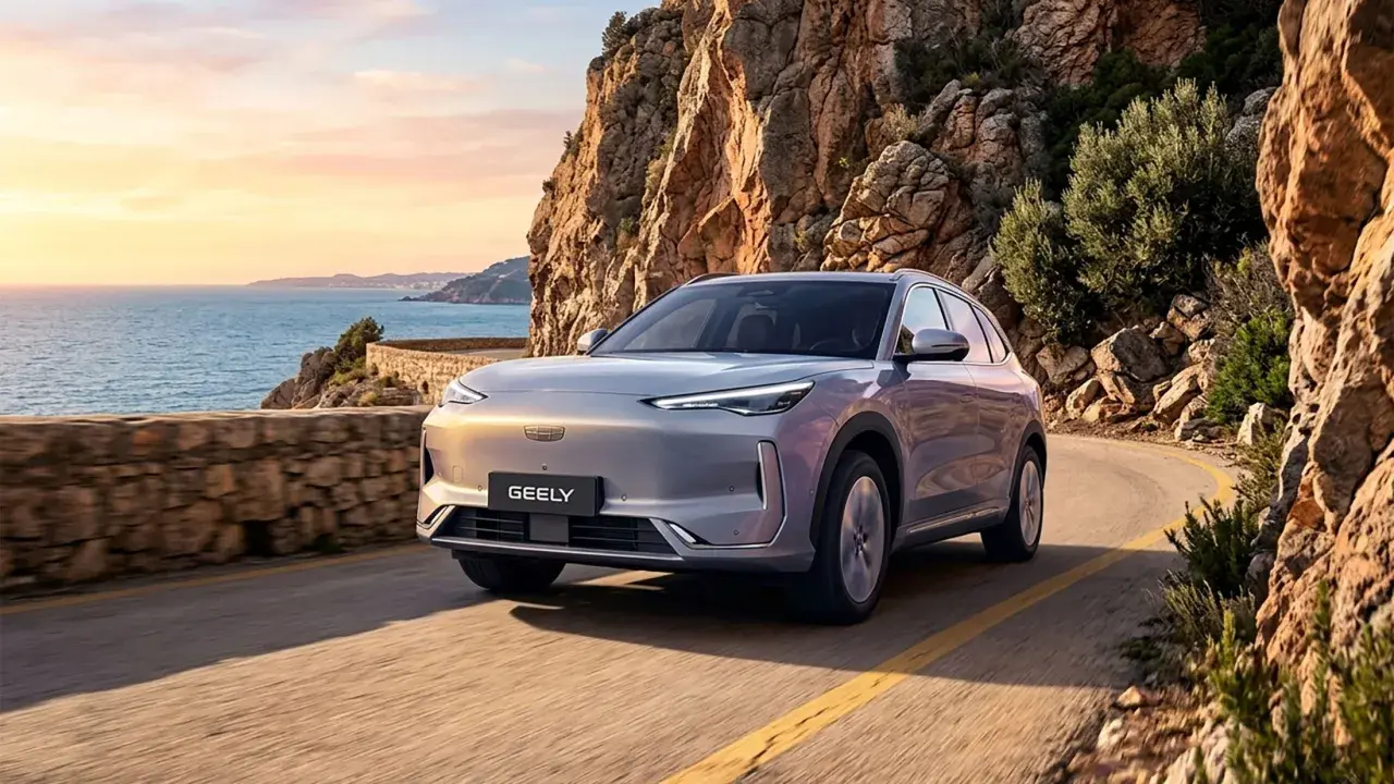 Un Geely plateado recorre una carretera costera en España al atardecer, con el mar Mediterráneo y acantilados rocosos de fondo.