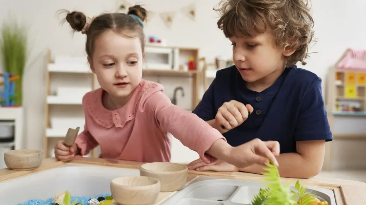 Dwoje dzieci bawi się w piaskownicy sensorycznej z niebieskim piaskiem i roślinami.