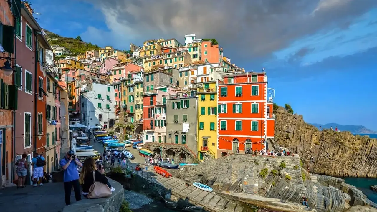 Bunte Häuserfronten der Cinque Terre Orte schmiegen sich an steile Felsen. Boote liegen im türkisfarbenen Wasser.