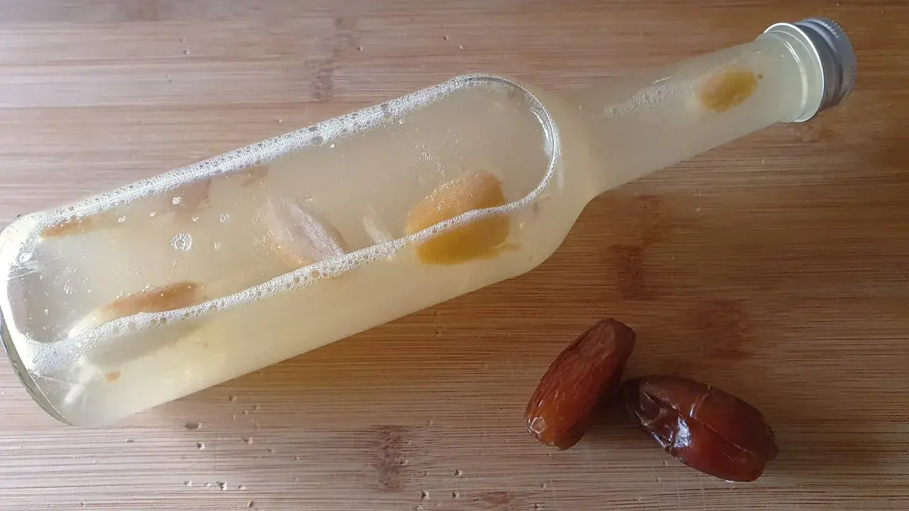 Flasche mit Flüssigkeit und Fruchtstücken, bereit zum Hefe selber machen. Daneben liegen zwei Datteln.