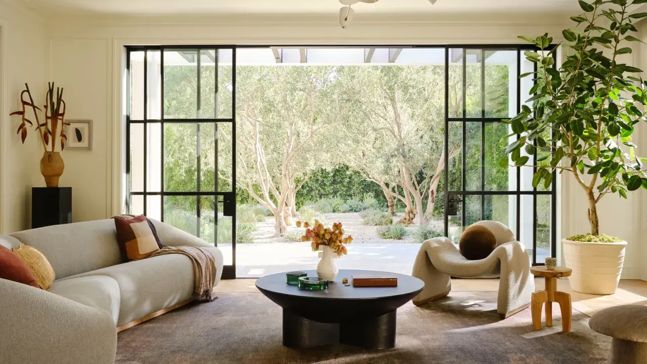 Salones modernos con sofá curvo, sillón acogedor y mesa de centro, conectados a un jardín soleado con olivos.