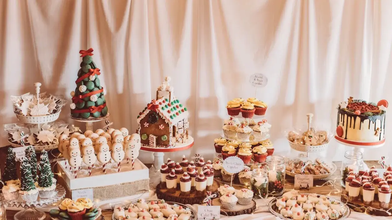 Mesa de dulces navideños con galletas de muñeco de nieve, casa de jengibre, pastel de árbol y cupcakes.