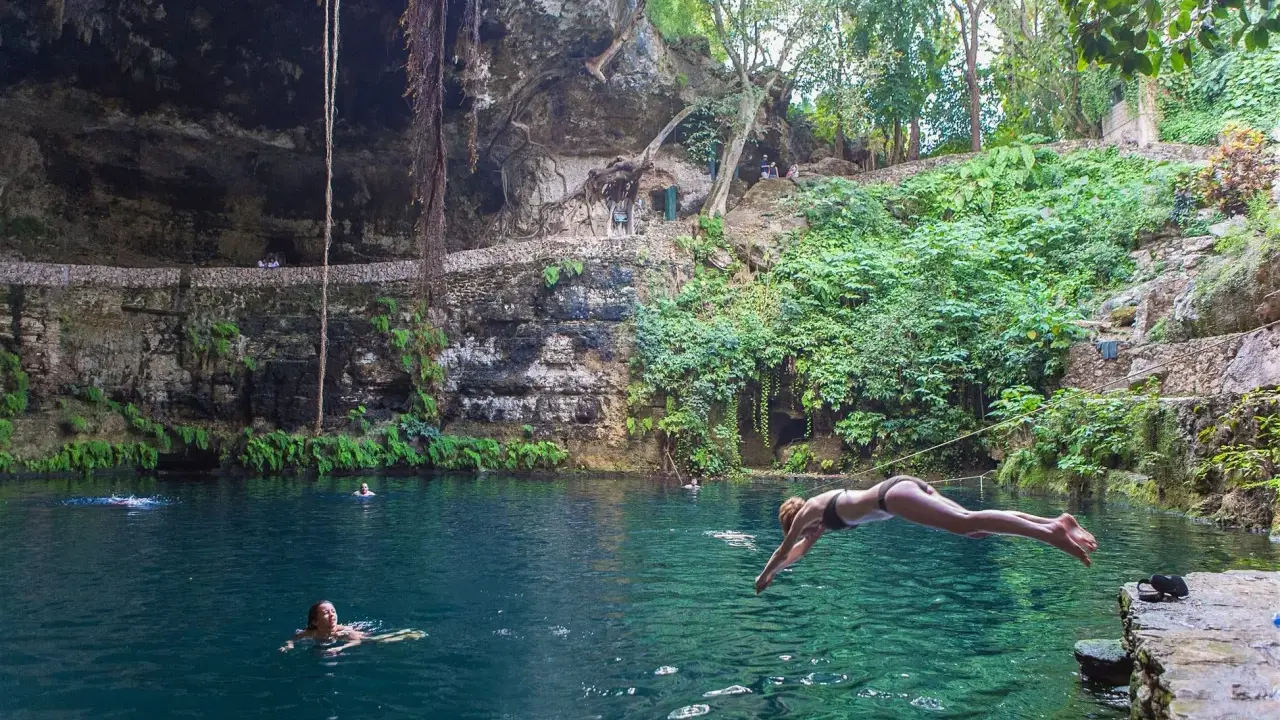 Una ragazza si tuffa nel **cenote Zaci**, un'oasi naturale con acque cristalline e vegetazione lussureggiante.