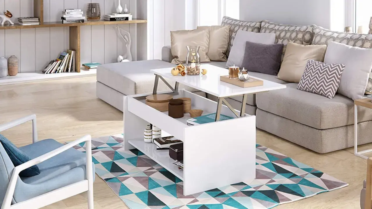 Mesa elevable pequeña blanca con compartimentos, junto a un sofá gris y una silla azul, sobre una alfombra geométrica.