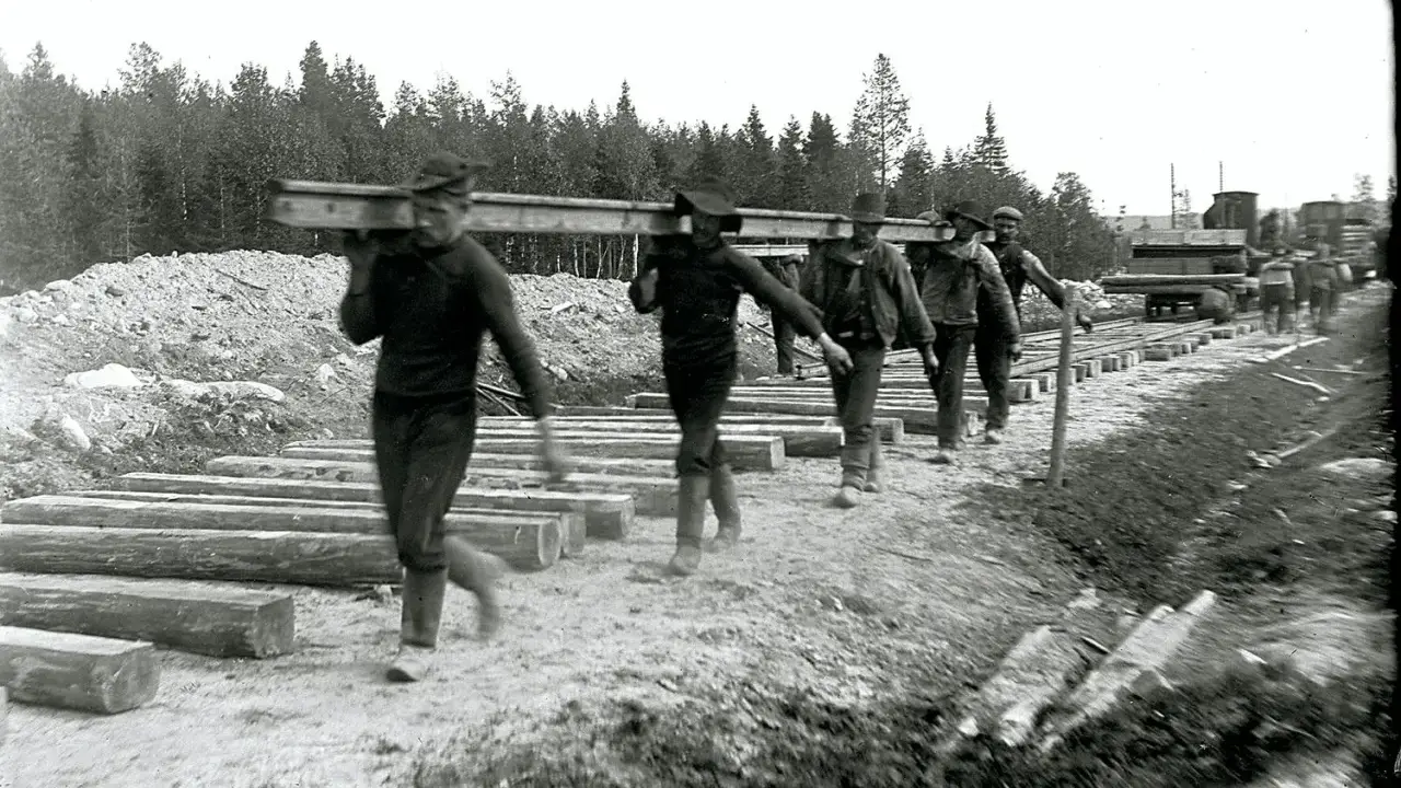 Rallarna i Sverige bär tunga stockar för järnvägsbygge.