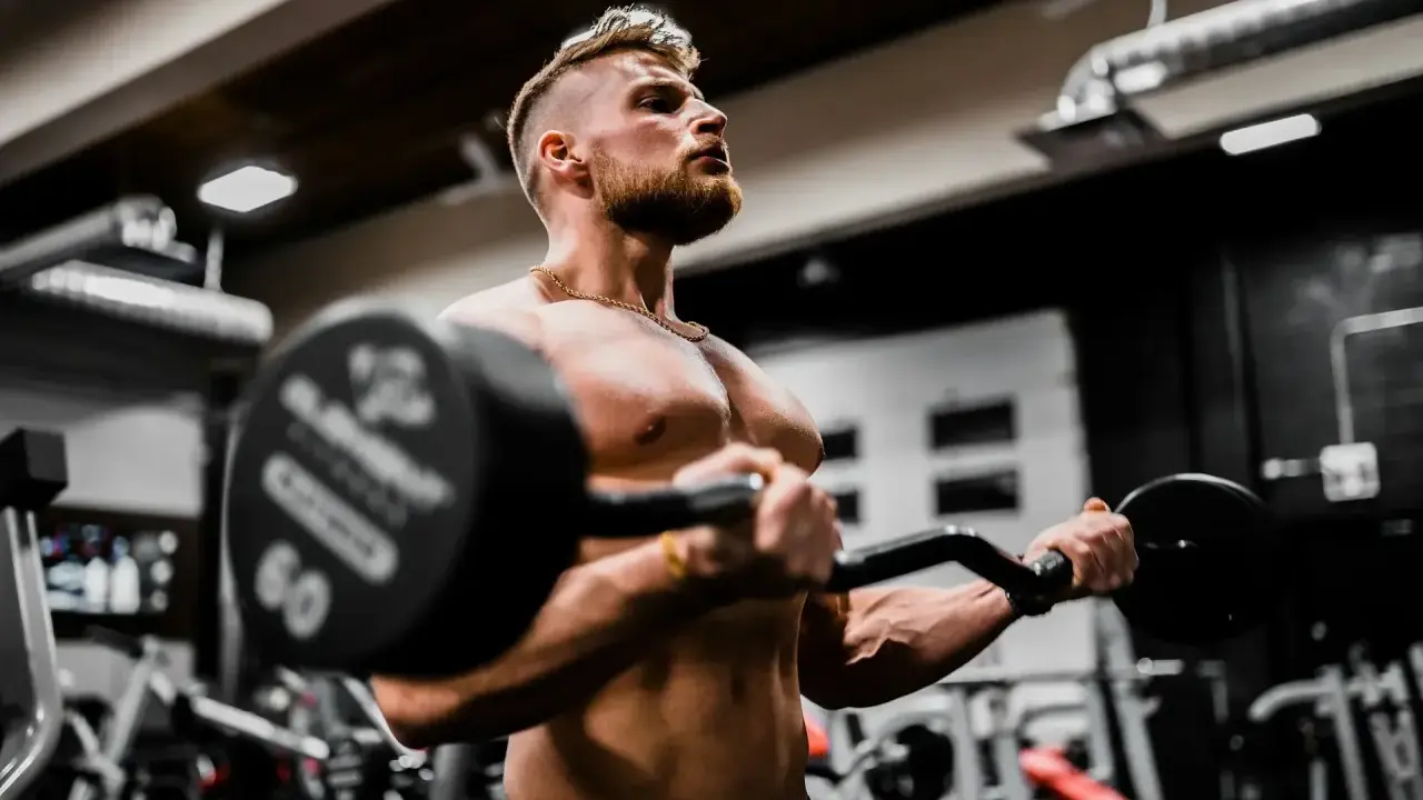 Mężczyzna ćwiczy biceps z ciężarem, wiedząc, że shake proteinowy co daje dla mięśni.