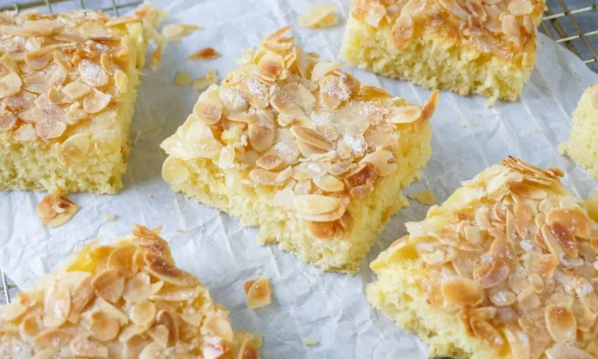 Saftiger Buttermilch Kuchen mit knusprigen Mandelblättchen und Zucker bestreut, auf Backpapier und einem Gitterrost arrangiert.