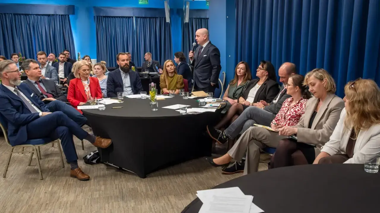 Grupa prawników siedzi przy okrągłych stołach podczas konferencji w Krakowie.