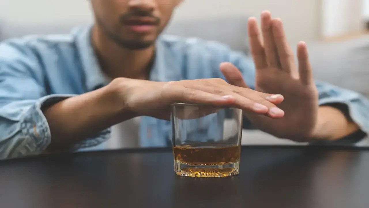 Mężczyzna odrzuca szklankę z alkoholem, symbolizując walkę z nałogiem. To obraz przymusowego leczenia alkoholika, który decyduje się na zmianę.