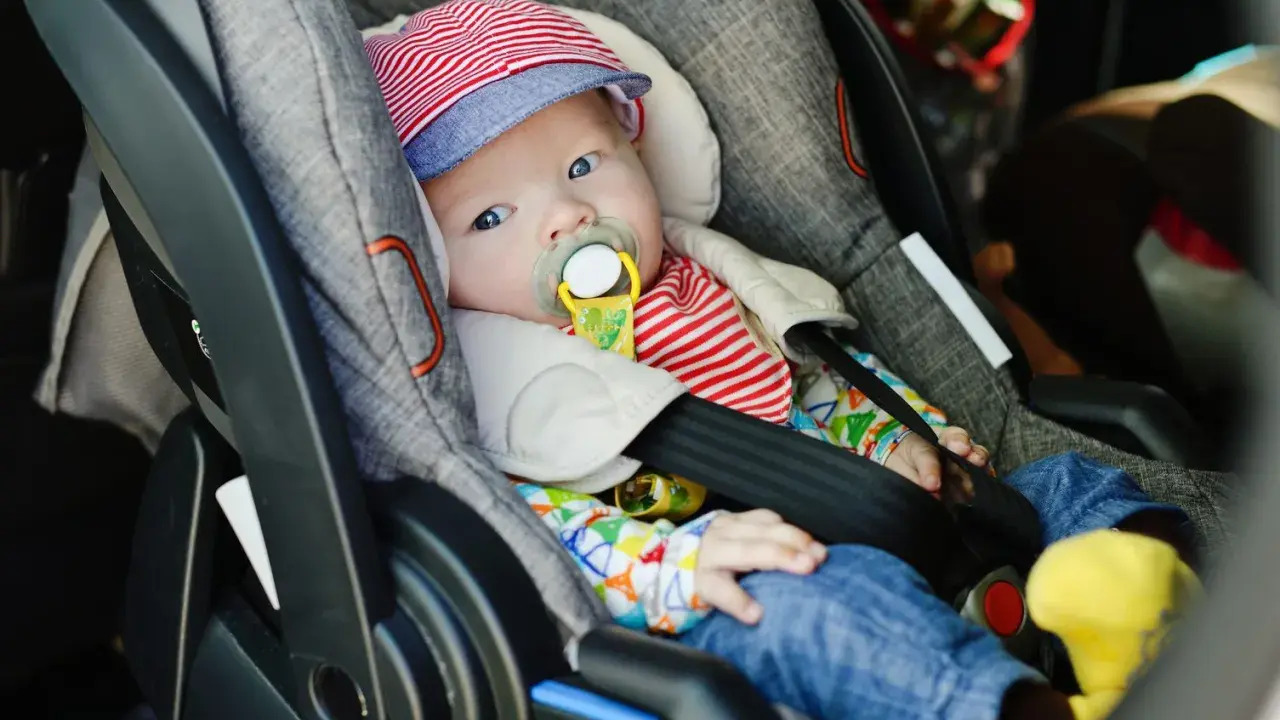 Baby mit Schnuller in Babyschale. Wann wechseln von Babyschale auf Kindersitz? Das Baby ist bereit für den nächsten Schritt.