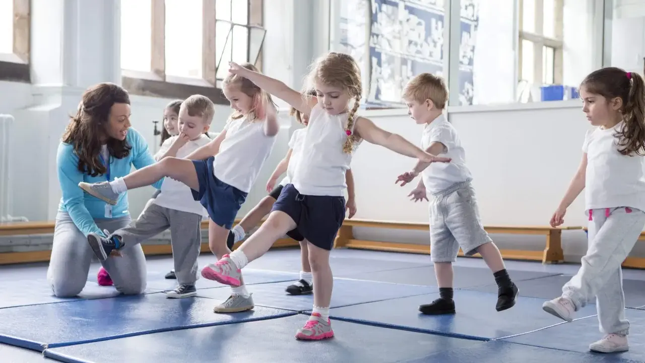 Niños aprendiendo movimientos de **deportes para niños** con una maestra en un gimnasio.