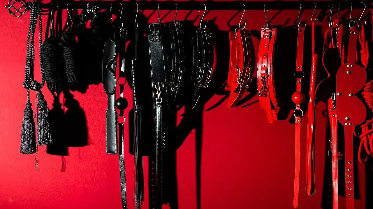 Kolekcja czarnych i czerwonych akcesoriów, takich jak bicze, kajdanki i maski, sugeruje fetysz seksualny.