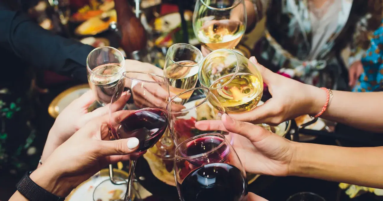 Ręce wznoszą kieliszki z winem, białe i czerwone, do toastu. Rozpoczyna się radosne świętowanie i trawienie alkoholu.