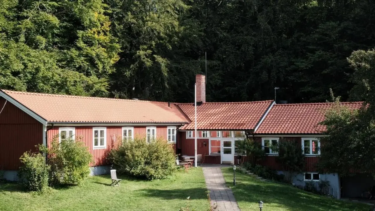Stocklycke vandrarhem, ett rött hus med tegeltak, omgivet av grönskande träd och en välskött gräsmatta.