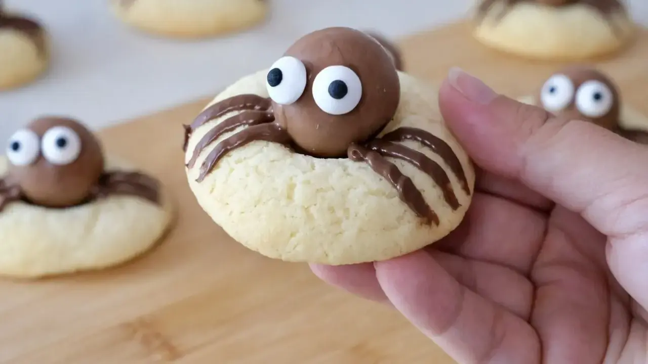 Des cookies araignée adorables avec des yeux en sucre et des pattes en chocolat, prêts à être dégustés.