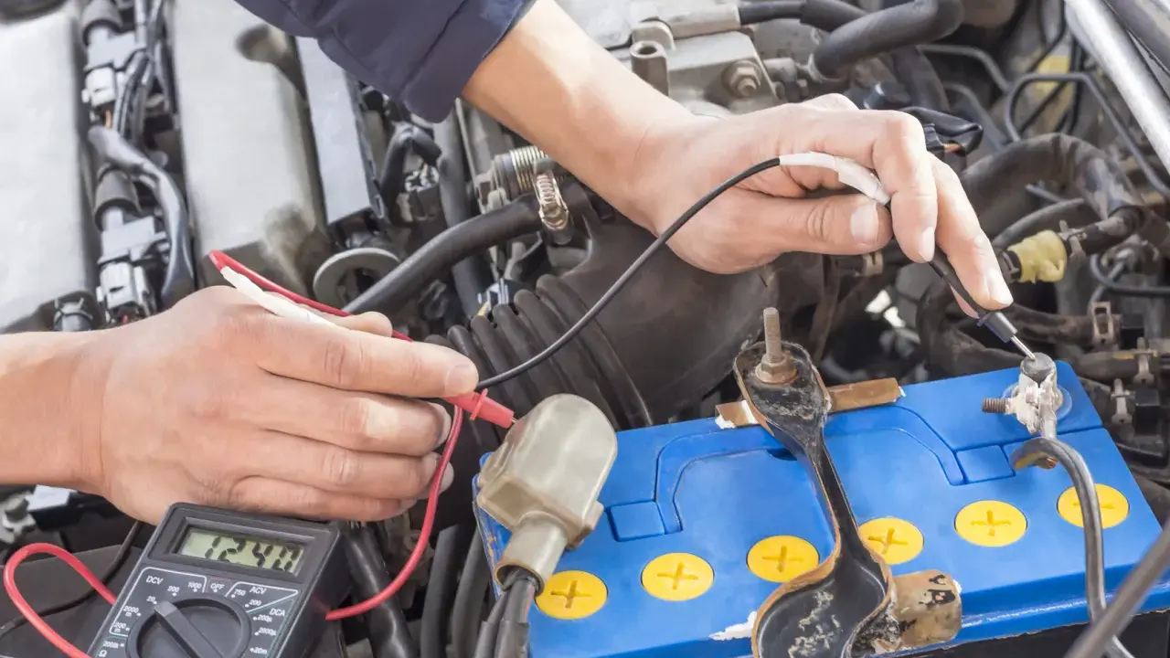 Mechanik sprawdza napięcie akumulatora za pomocą multimetru. Wynik 12.48V wskazuje na jego stan.