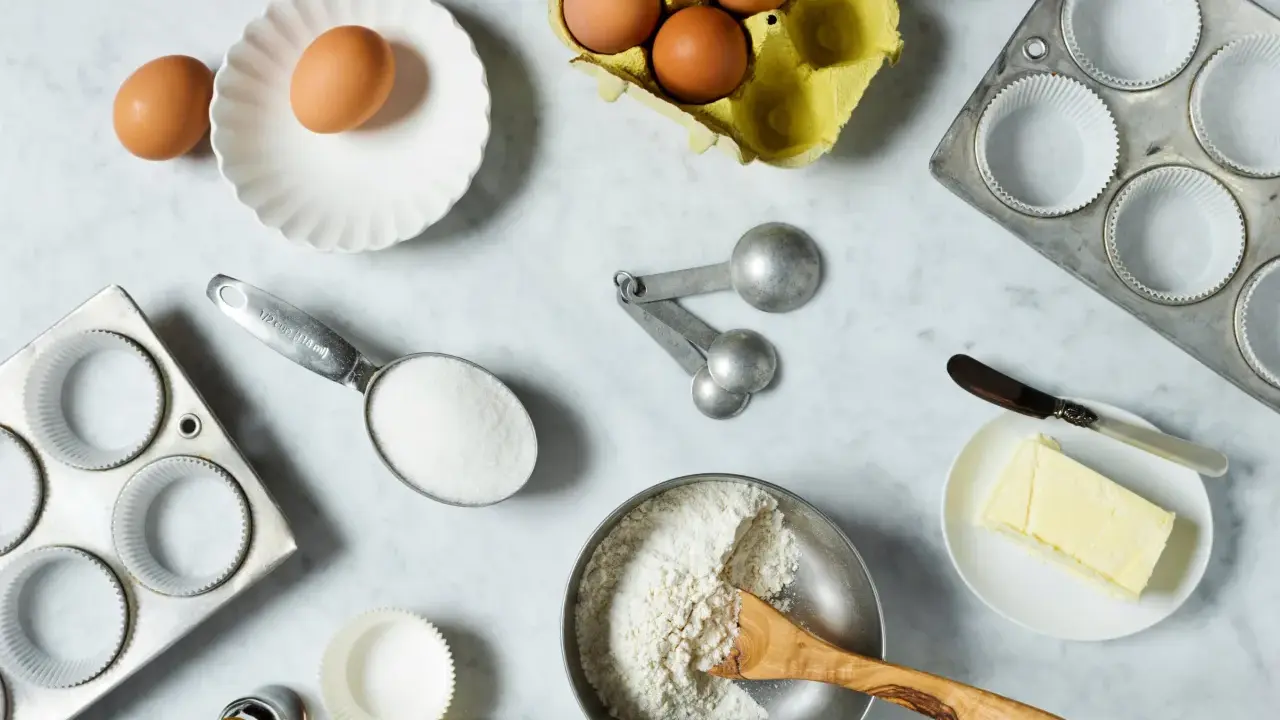 Backzutaten: Eier, Mehl, Zucker, Butter, Muffinförmchen und Messlöffel im amerikanischen Maßsystem.