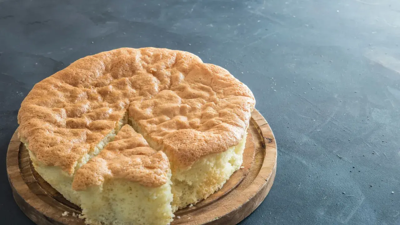 Un gâteau raté, un peu affaissé, sur une planche en bois. Sa texture est spongieuse et sa croûte dorée.