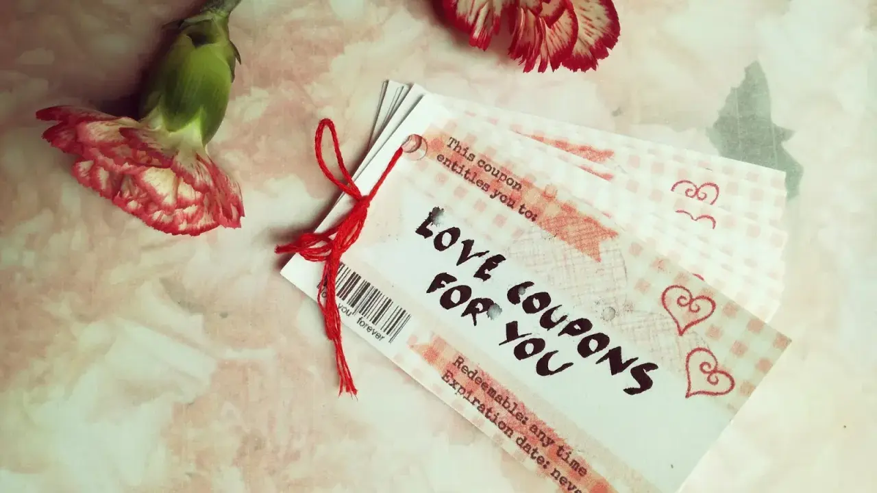 Papierowa rocznica uczczona kuponami miłości. Dwa kwiaty goździka i stosik kuponów "Love Coupons for You" na różowym tle.