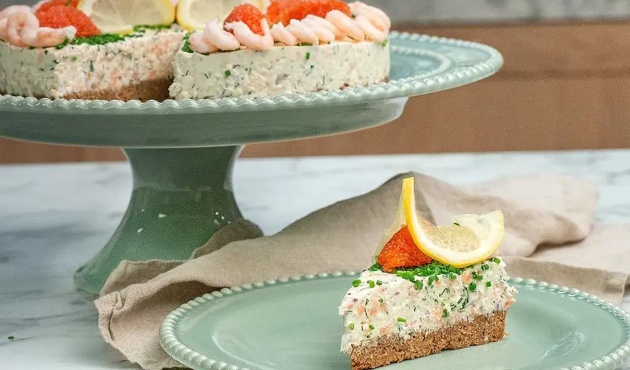 En läcker laxtårta på kavring, dekorerad med räkor, rom och citron. En bit serveras på en mintgrön tallrik.