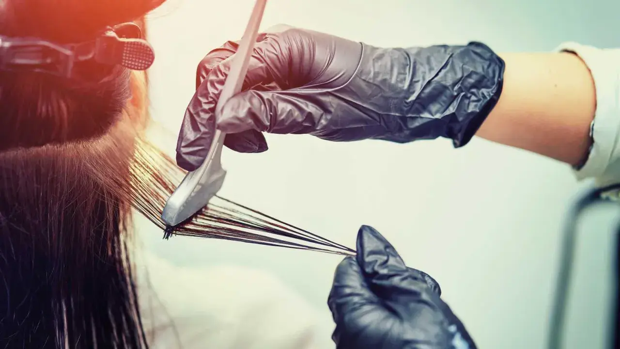 Mani guantate applicano tinta ai capelli. Scopri quanto dura una tinta dal parrucchiere per un colore impeccabile.