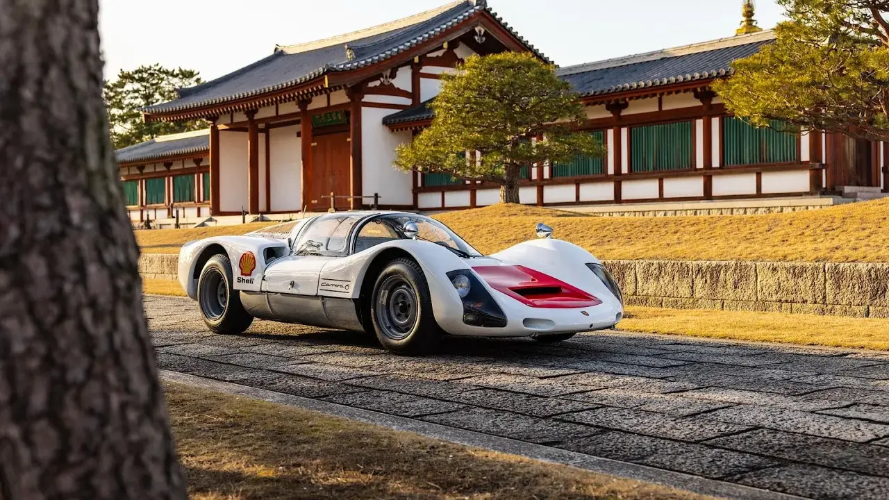Ein weißer Porsche 966 mit roten Akzenten steht vor einem traditionellen japanischen Gebäude.