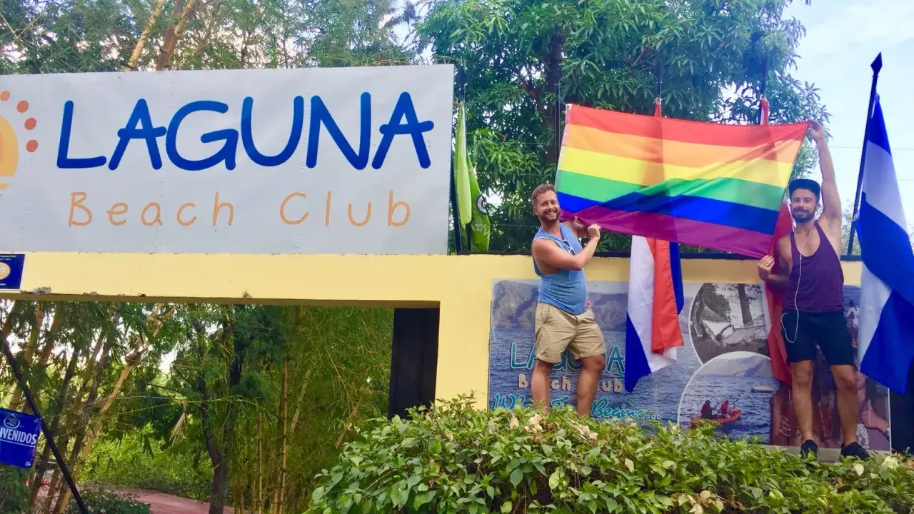 Two men proudly hold a rainbow flag at Laguna Beach Club, celebrating gay pride in Guatemala.