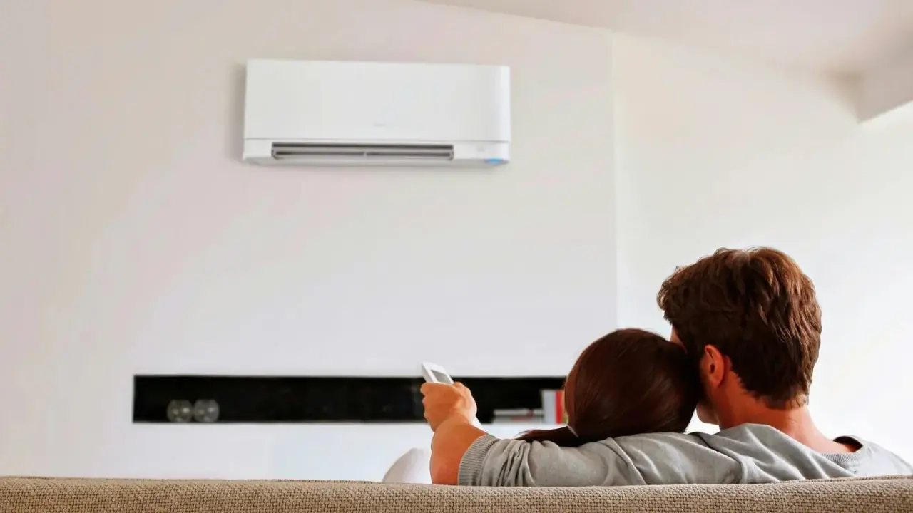 Pareja relajada en el sofá, disfrutando del confort que ofrece un **split aire acondicionado** en la pared.