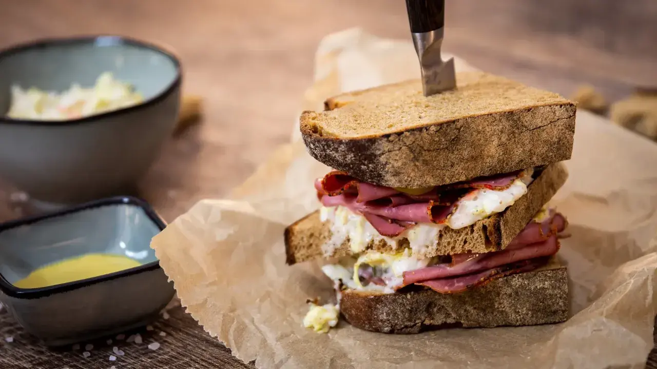 Ein üppiges Pastrami-Sandwich mit Röstbrot, serviert mit Beilagen wie Krautsalat und Senf.