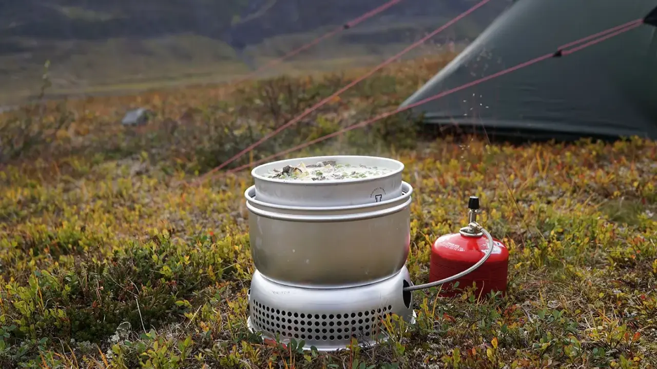 Matlagning på ett esbit kök i fjällen. En kastrull med mat värms upp bredvid ett tält.
