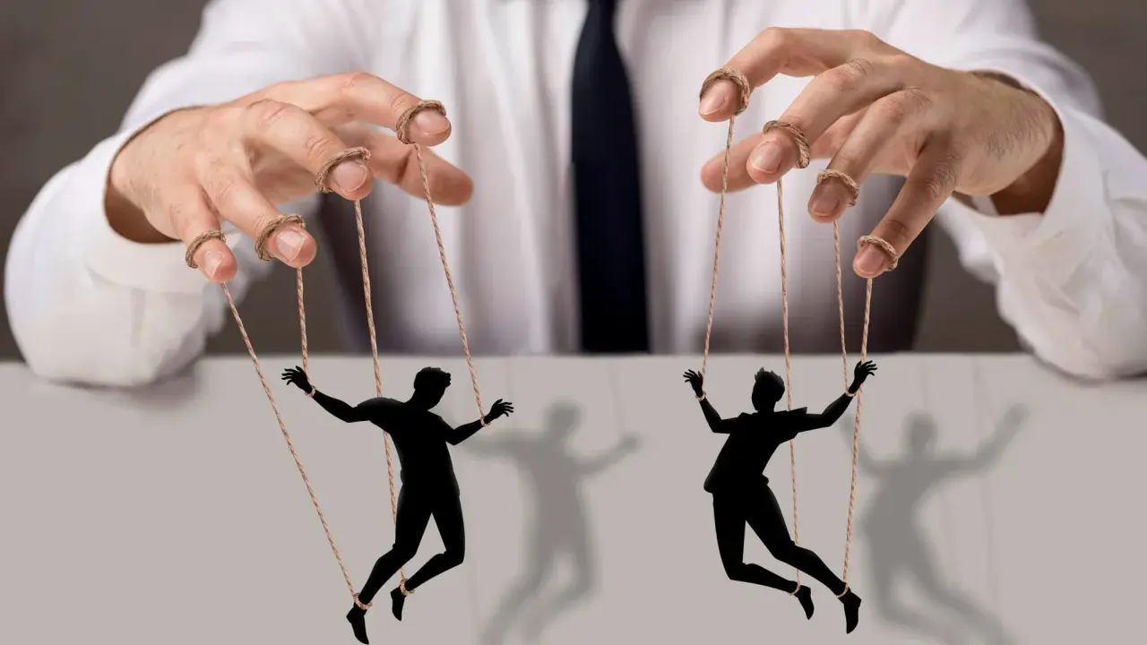 Dłonie w białej koszuli i krawacie sterują ludzikami jak marionetkami. To obraz siły perswazji, co to znaczy?