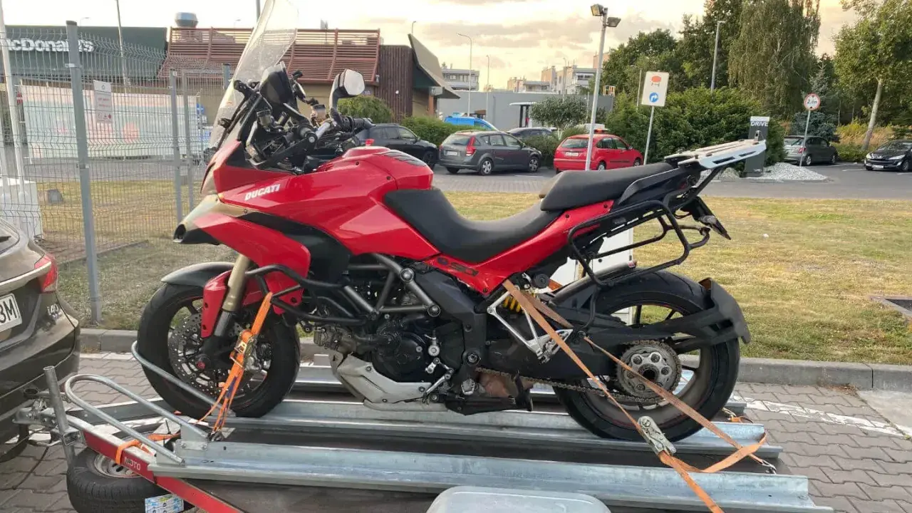 Czerwony Ducati na przyczepie, zabezpieczony pasami do transportu. Gotowy do drogi.
