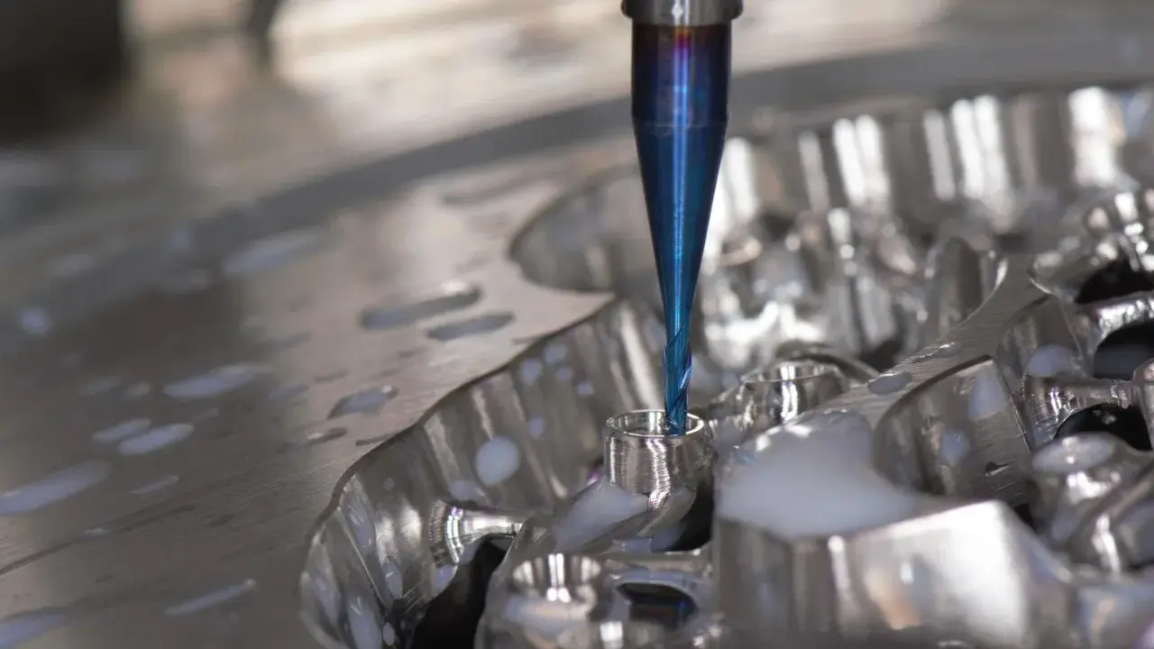 Fresa blu lavora un pezzo metallico, creando dettagli precisi. La cam meccanica è in azione, con liquido refrigerante che schizza.
