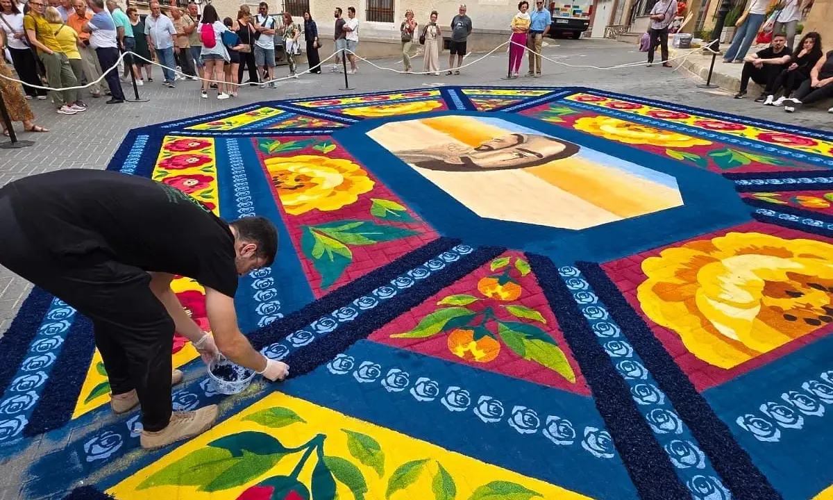 Un hombre finaliza una de las alfombras de serrín de Elche de la Sierra, con un retrato central y motivos florales y frutales.