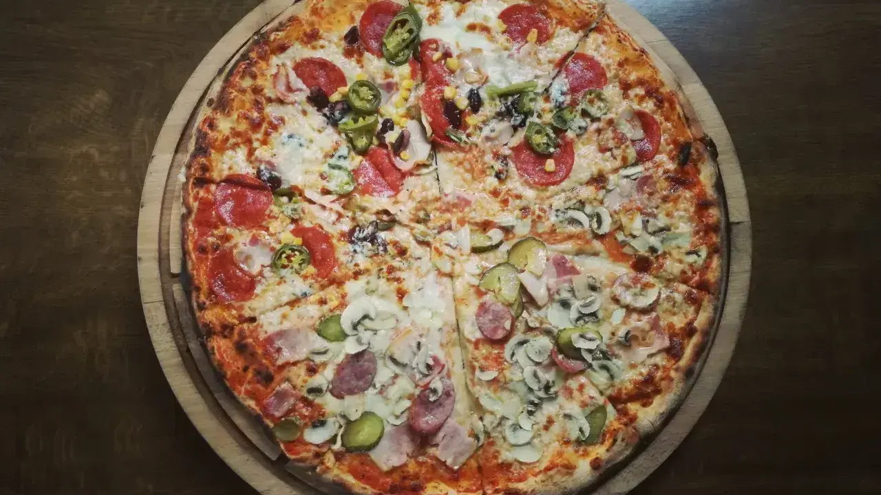 Cała pizza z różnymi dodatkami: salami, pieczarki, kukurydza, papryczki jalapeno i ogórek.