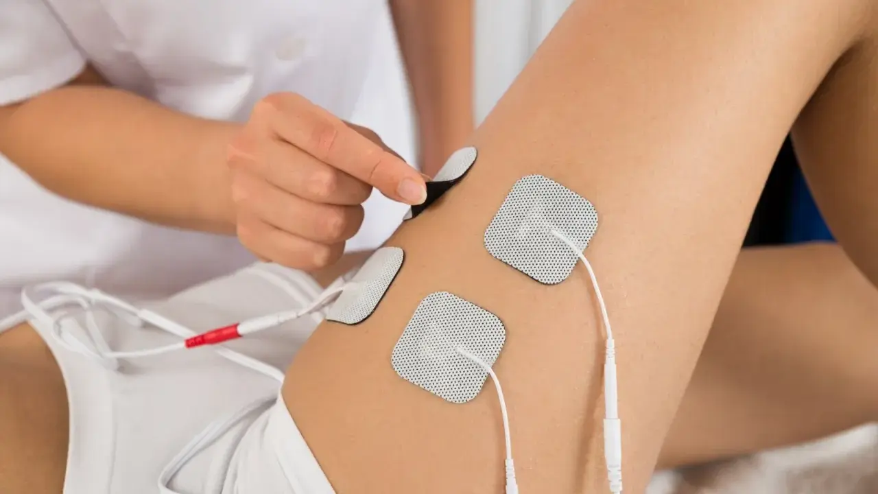 Terapeuta umieszcza elektrody na udzie pacjenta, przygotowując do zabiegu elektrostymulacji.