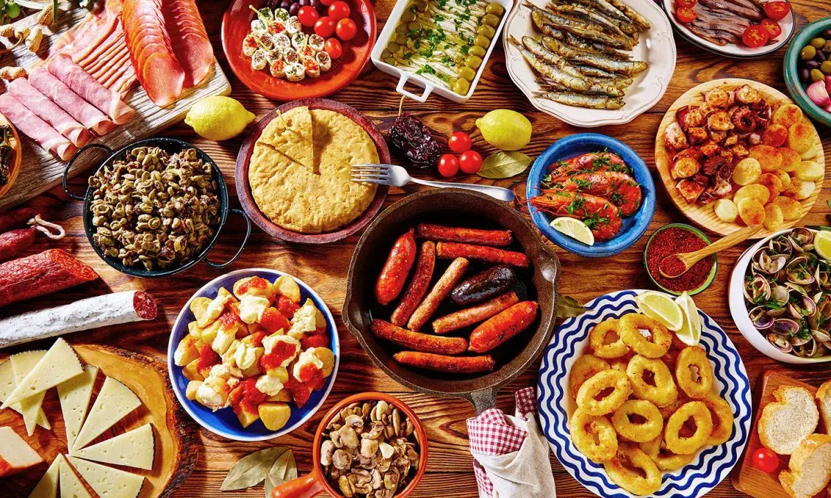 Tapas co to? Kolorowy stół pełen hiszpańskich przekąsek: kiełbaski, krewetki, owoce morza, tortilla, sery i wędliny. Prawdziwa uczta!