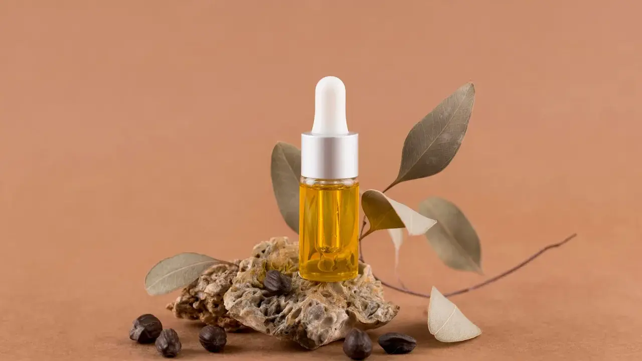 Flacon d'huile dorée, posé sur une pierre avec des graines et des feuilles séchées. Un élixir naturel pour des cheveux éclatants, comme l'huile de ricin cheveux.