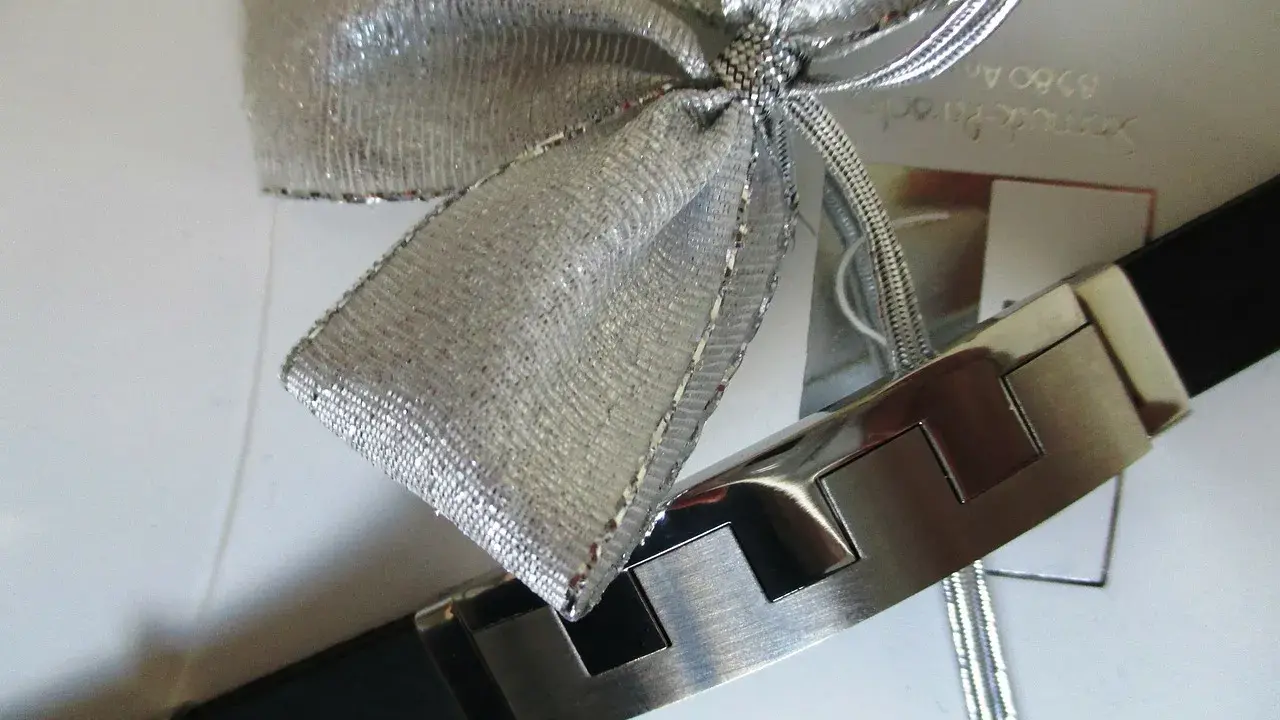 Elegancka bransoleta z czarnym paskiem i metalowymi elementami, ozdobiona srebrną kokardą. Idealnie pokazuje, jak zapakować biżuterię na prezent.