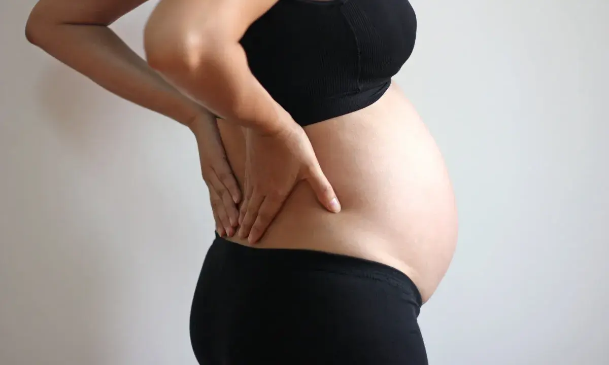 Gravid kvinna med handen på ryggen, upplever ont i ljumsken.