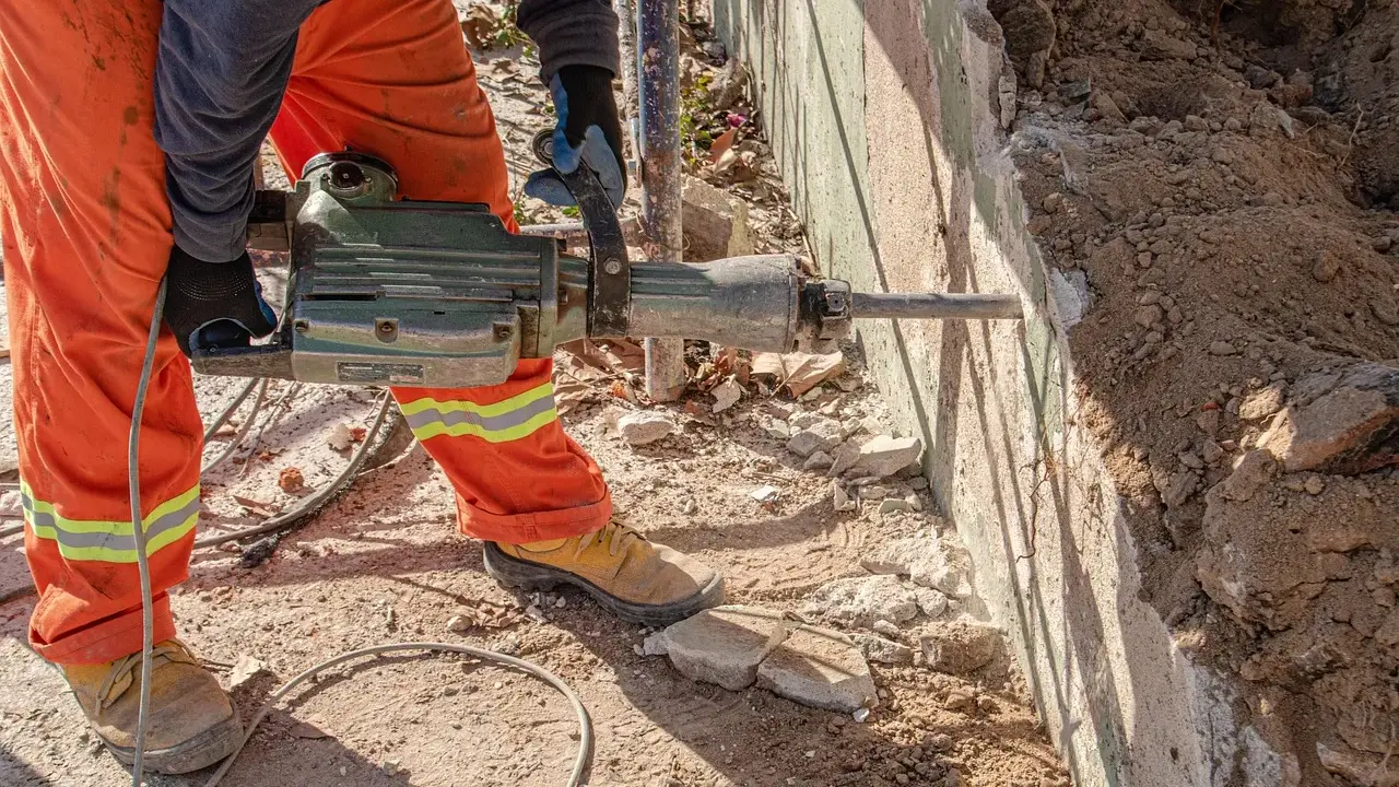Trabajador con martillo neumático realiza demolición manual de muro de hormigón.