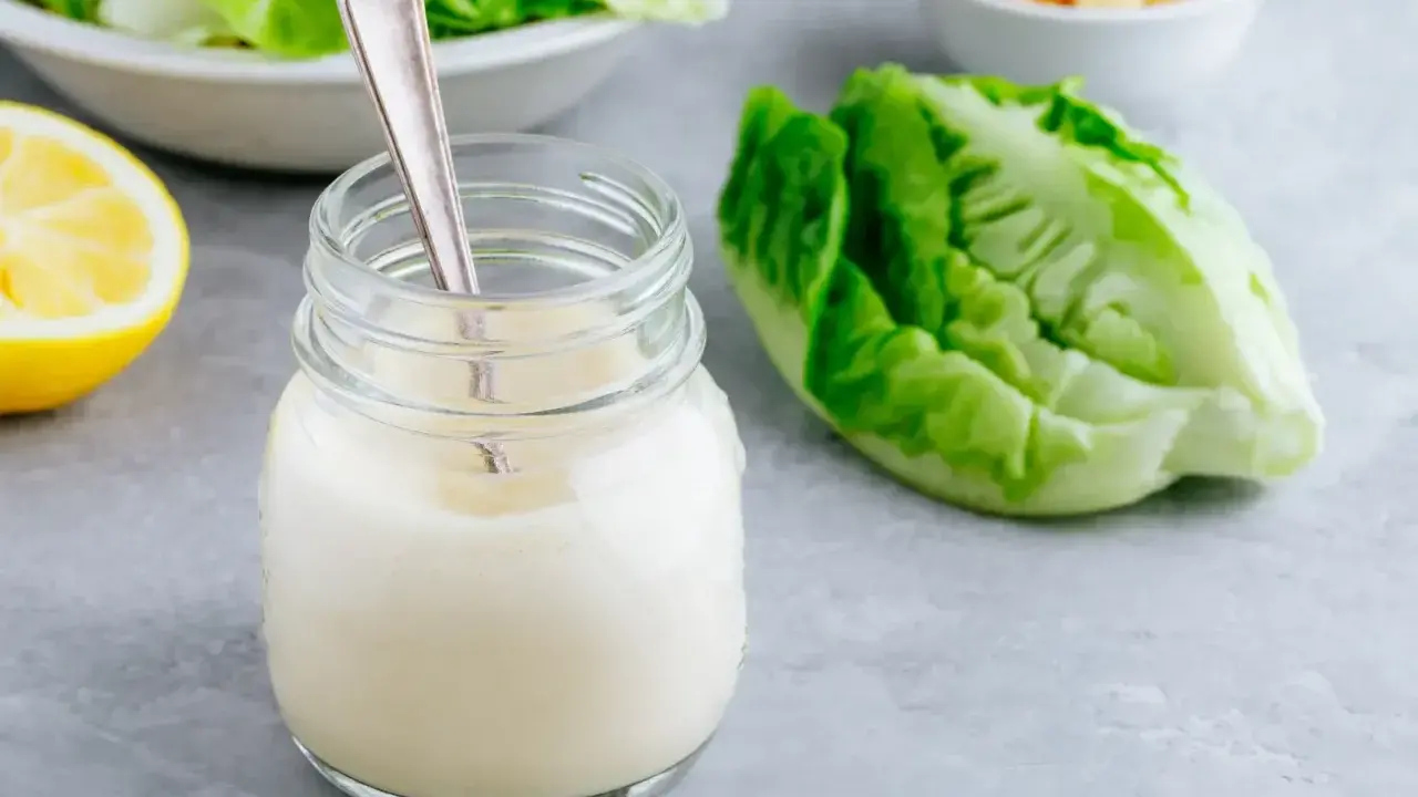 Un pot de vrai sauce césar crémeuse, avec une feuille de laitue romaine et un quartier de citron.