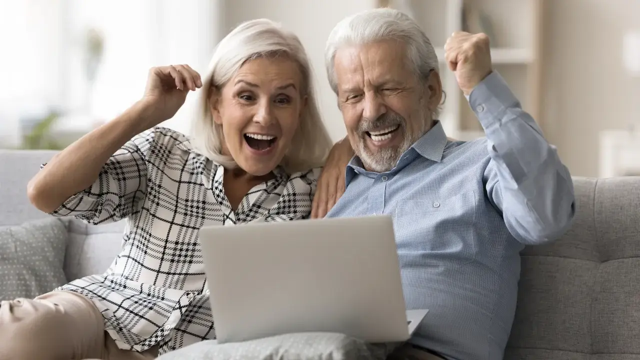 Szczęśliwi seniorzy sprawdzają na laptopie przeliczenie emerytury rocznik 1949 do 1953.