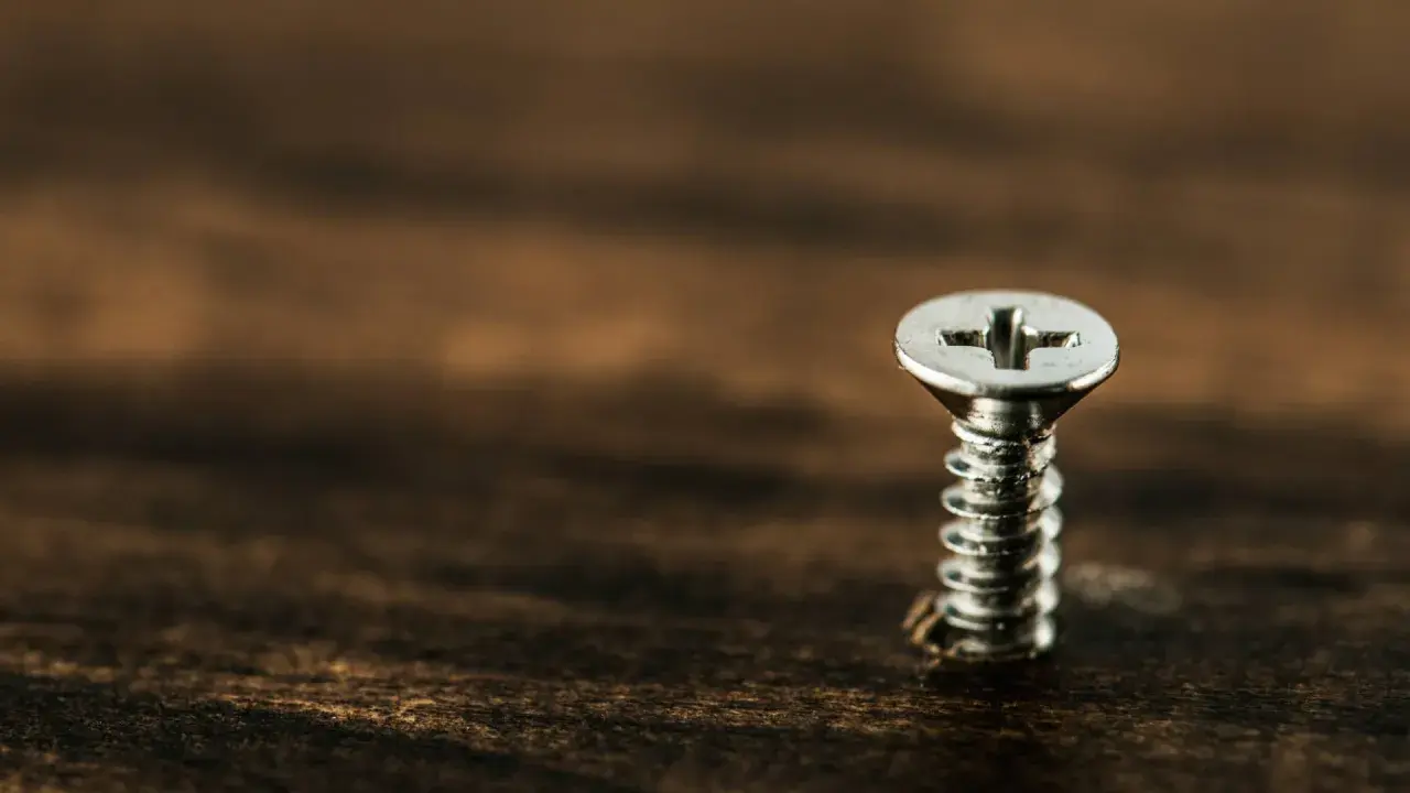 Un tornillo plateado sobre madera oscura. Para sacarlo, gira hacia la izquierda.