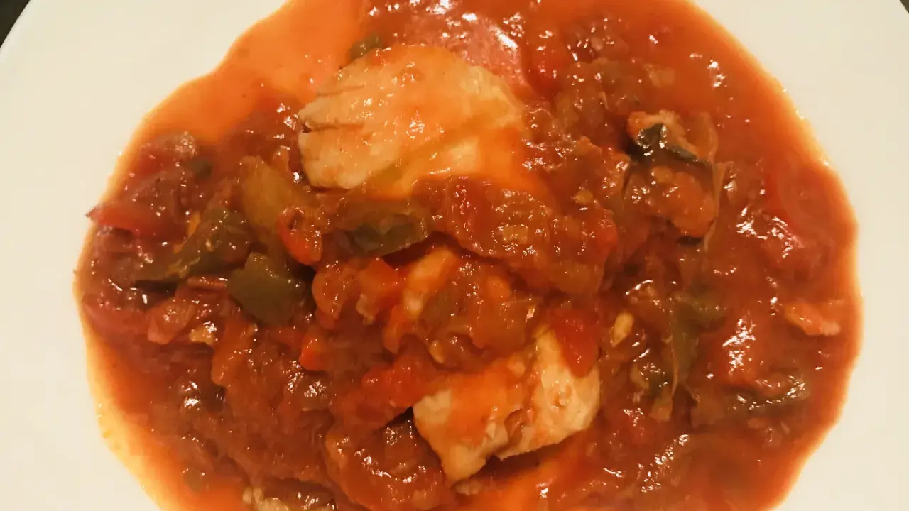 Un plato de urta a la roteña, con trozos de pescado blanco en una salsa roja de tomate y verduras.