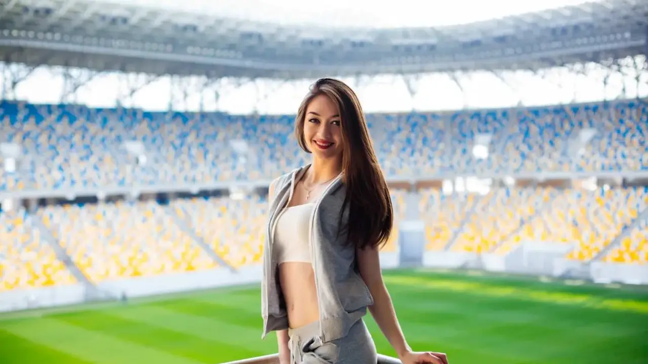 Uśmiechnięta dziewczyna w sportowym stroju na tle stadionu. Idealny przykład, jak się ubrać na mecz, by czuć się komfortowo i stylowo.