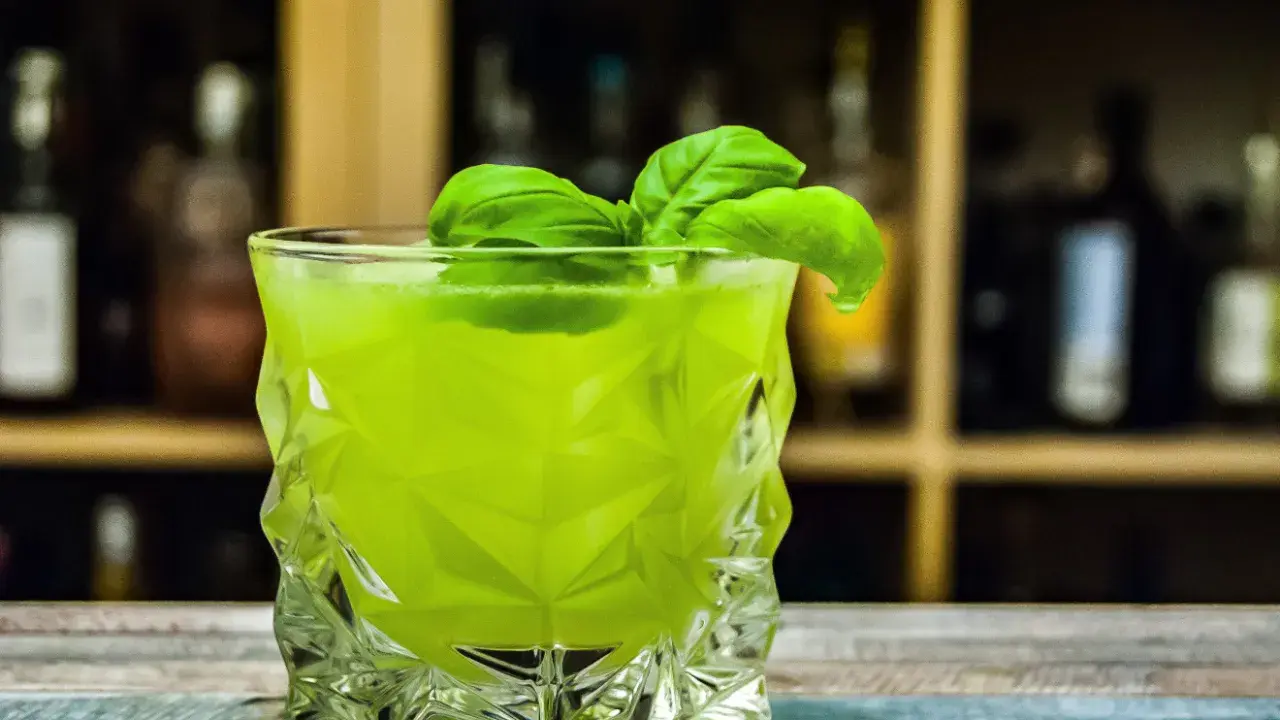 Orzeźwiający drink z likierem miętowym, ozdobiony listkami bazylii, w szklance o geometrycznym kształcie.